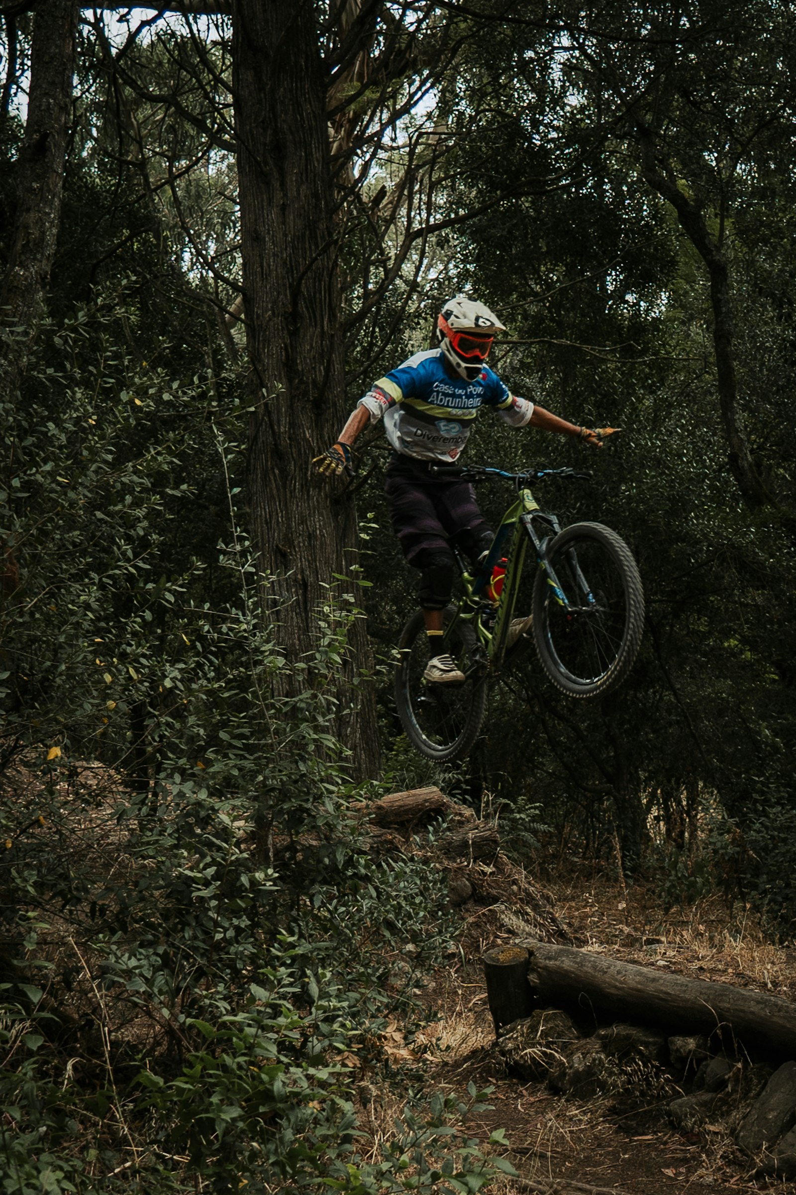 Un pilote de VTT équipé franchissant un passage technique en descente sur un sentier forestier